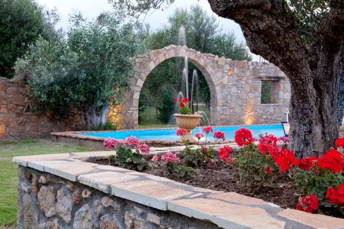 Πέτρινη καμάρα πάνω από το νερό, με κόκκινα λουλούδια μπροστά